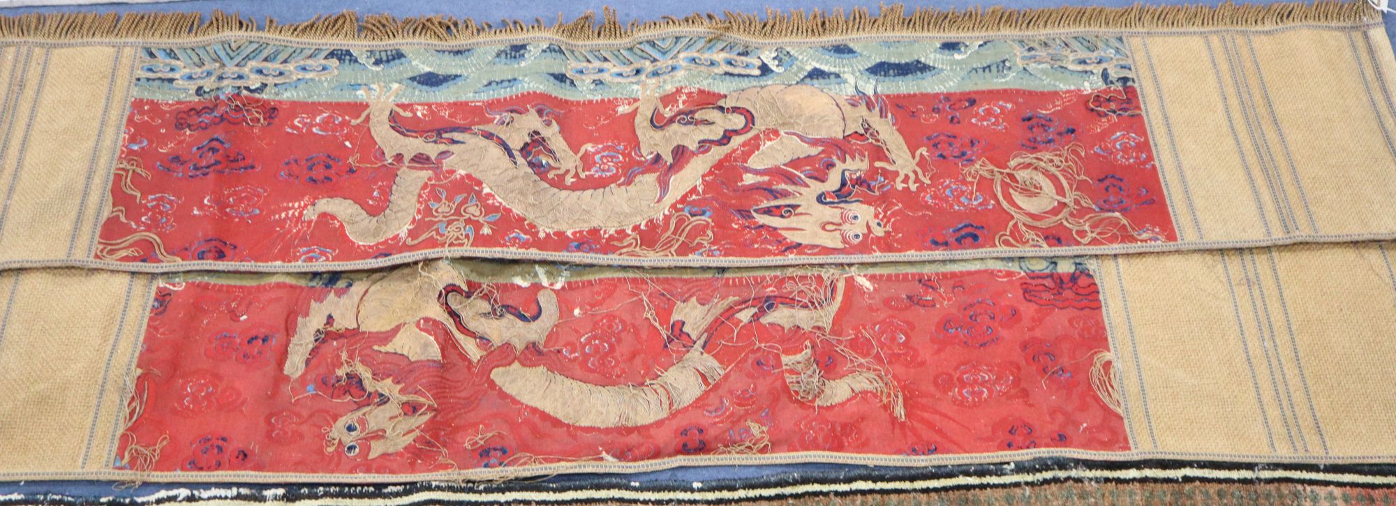 A pair of Antique Chinese silk and gold threadwork panels depicting dragons over waves, 38 x 150cm and 38 x 130cm, distressed and now